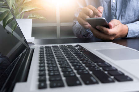 Cropped shot Silhouette of a man's hands using a laptop, business man hands busy using laptop at office desk, typing on computer sitting wooden table, phone on table, filter sunの写真素材