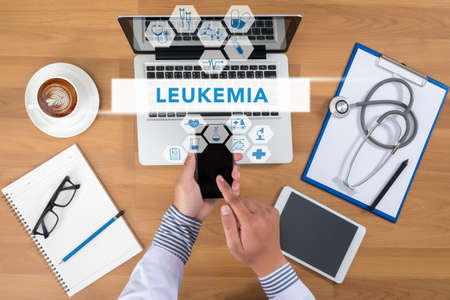 LEUKEMIA CONCEPT Doctor working at office desk and using a mobile touch screen phone, computer and medical equipment all around, top view, coffeeの写真素材