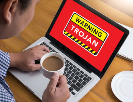 Warning Trojan Concept Businessman at work. Close-up top view of man working on laptop while sitting at the wooden desk , coffeeの写真素材