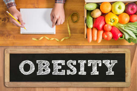 OBESITY notebook with fresh vegetables and  on a wooden table,の写真素材