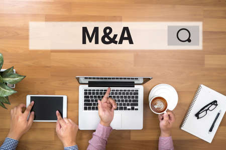 M&A (MERGERS AND ACQUISITIONS) Two Businessman working at office desk and using a digital touch screen tablet and use computerの写真素材