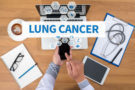 LUNG CANCER  Doctor working at office desk and using a mobile touch screen phone, computer and medical equipment all around, top view, coffeeの写真素材