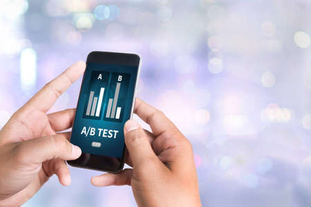 A/B TEST person holding a smartphone on blurred cityscape backgroundの写真素材