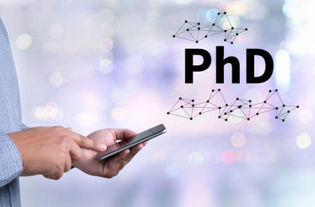 PhD Doctor of Philosophy Degree Education Graduation person holding a smartphone on blurred cityscape backgroundの写真素材