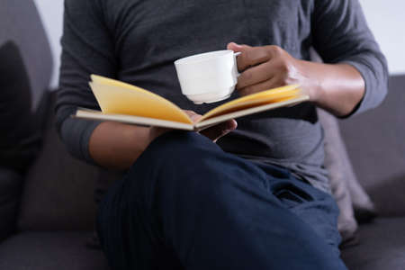 man reading a book and holding cup of coffee Sit Read Knowledge