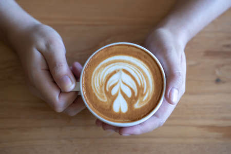 women  Holding coffee cup, wooden table  cafe while having coffeeの写真素材