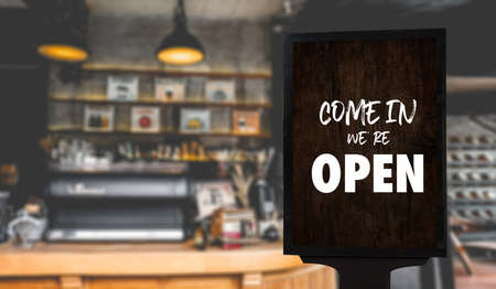 Come in Weâre Openâ on cafe waiter standing in front of coffee shop vintage retro sign Open sign at coffeeの写真素材