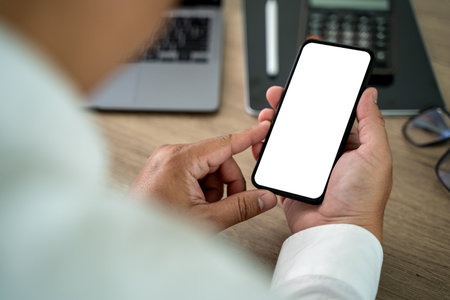 Close-up man hand mock up using phone blank screen background is blurred in office in communicationの写真素材