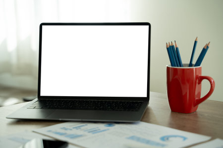 A businessman is using a modern laptop on a white desk in a bright office, typing on a keyboard while viewing a blank screen, showcasing technology and communication.の写真素材