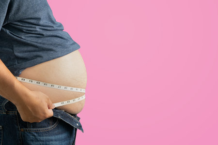 The dangers of the disease of obese people with a potbelly An overweight adult holds their belly, stressed about unhealthy eating and excess weightâseeking a healthier lifestyle.の写真素材