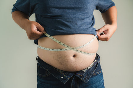 An overweight man holds his belly, unhappy with his unhealthy lifestyle, seeking weight loss and better fitness habits. Big fat man overweightの写真素材