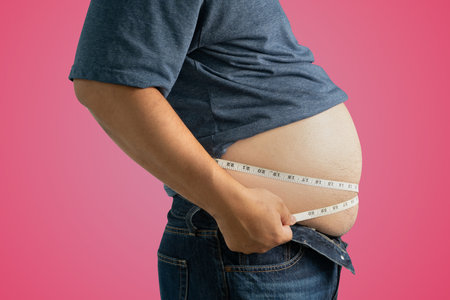 The dangers of the disease of obese people with a potbelly An overweight adult holds their belly, stressed about unhealthy eating and excess weightâseeking a healthier lifestyle.の写真素材