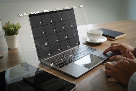A 2025 calendar person using laptop with digital calendar overlay screen workspace with smartphone notebook coffee cup and plant modern officeの写真素材