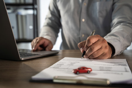 An insurance on paperwork assurance person gray shirt signing document with pen, small red toy car paper, and laptop desk, indicating businessの写真素材