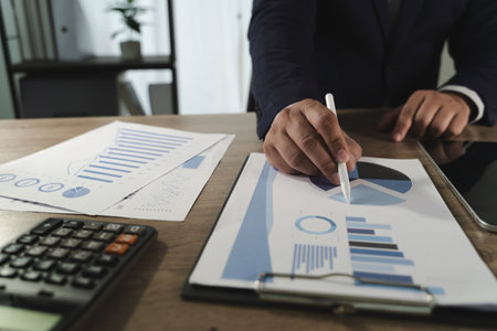 A paperwork report file with charts person business suit analyzing financial charts and graphs paper, with calculator and tablet wooden deskの写真素材