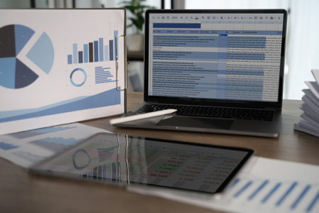 A report file modern workspace with laptop displaying spreadsheet, tablet showing data, and presentation board with charts, indicating businessの写真素材