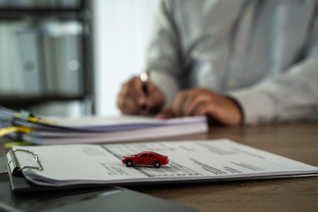 An insurance on paperwork assurance person gray shirt is signing documents desk with small red toy car placed top of papers, suggesting car insuranceの写真素材