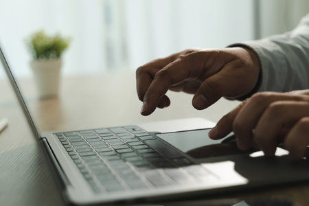 A call center person using laptop computer bright room with natural light and potted plant background. person is typing or navigating keyboardの写真素材