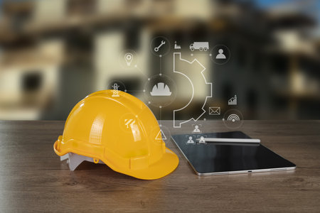An engineer architect industry 4.0 image shows yellow safety helmet placed wooden table next to tablet with digital icons and graphics floating aboveの写真素材