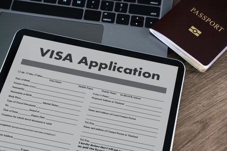 A visa application digital tablet displaying visa application form placed wooden desk with passport and laptop keyboard background, suggestingの写真素材