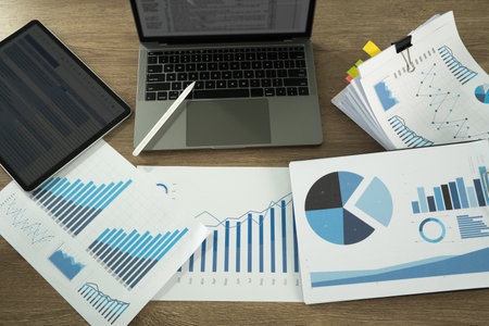 A report document image shows workspace with various financial charts, graphs, laptop, and tablet, indicating data analysis or business planningの写真素材