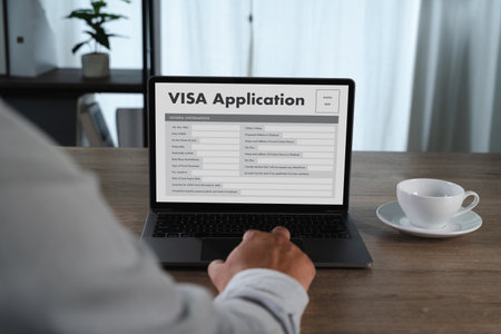 A visa application person filling out visa application form laptop desk bright room with cup of coffee nearby. scene depicts online applicationの写真素材