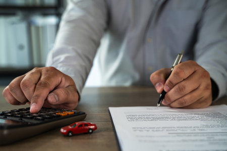 An insurance on paperwork assurance person working desk with calculator, pen, and documents, possibly reviewing financial or legal papersの写真素材