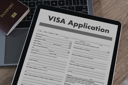 A visa application digital tablet displaying visa application form with passport and laptop background, wooden surface, representing travelの写真素材