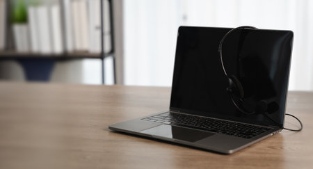 An all center and customer service sleek laptop with headset placed wooden table bright, modern workspace with natural light and bookshelvesの写真素材