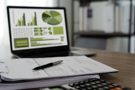 A report file eco friendly image shows desk with financial documents, pen, and laptop displaying charts and graphs, indicating business or financialの写真素材