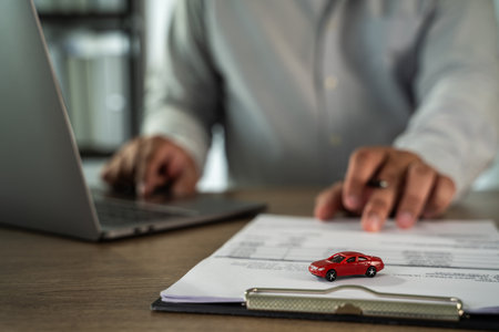 An insurance on paperwork assurance person is working desk with laptop, pointing document with small red car model top, indicating discussion aboutの写真素材
