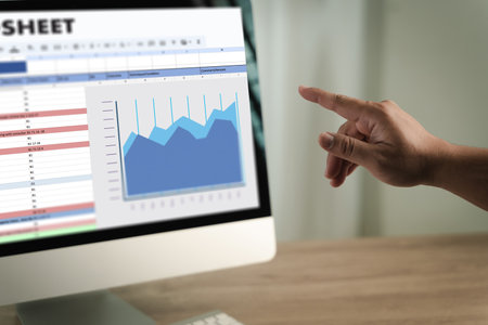 A man working on excel person pointing at computer screen displaying spreadsheet and line graph, analyzing data and trends in professional settingの写真素材