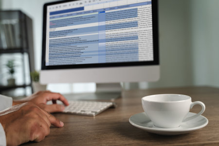 A man working on excel person working desk with computer and coffee cup, modern office environment, with blurred background, showing busy scheduleの写真素材