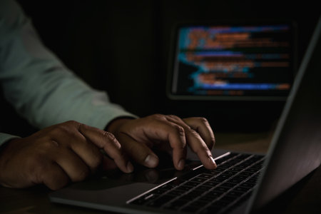 Close-up of programmer typing code on laptop with blurred screen of programming in background,...