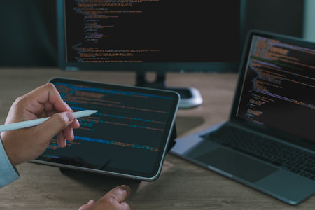 Close-up of programmer freelance working on tablet and laptop with code on screen, modern software...