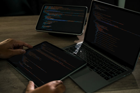 Programmer writing Development Website design code at a desk with laptop and tablet dark workspace, hands on keyboard, css and html modern software development, tech projects.の写真素材