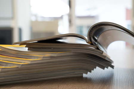 Close up of stacked open magazines showing curved pages and blurred background. Publishing,...
