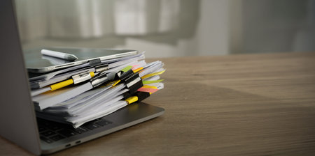 stacked documents compliance with stack of files and tabs on laptop , representing due diligence...