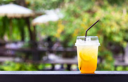 Ice honey lemon soda yellow in plastic glass put on table with background of  tree and cafe. Herbal drink for health.の写真素材