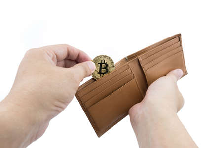 Bitcoin. Man hand input gold bitcoin into brown wallet on isolated backgroundの写真素材