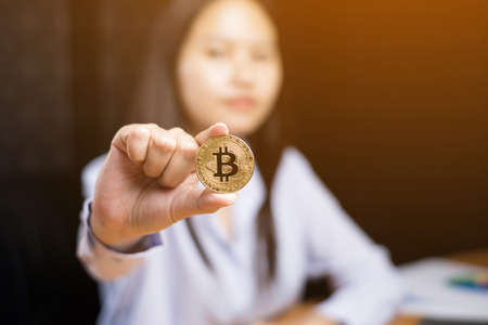 Business woman's hand holding a gold bitcoin at office with sun effect.の写真素材