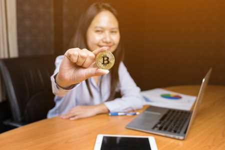 Business woman's hand holding a gold bitcoin at office with sun effect.の写真素材