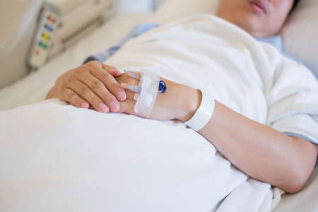 Closeup of hands with intravenous (IV) man patient in hospital bed.の写真素材