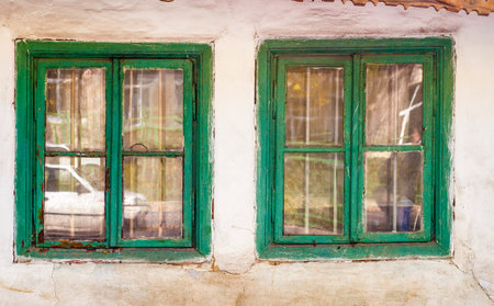 Two old green wooden window frames set in a white, weathered wall. The paint is chipping and the...