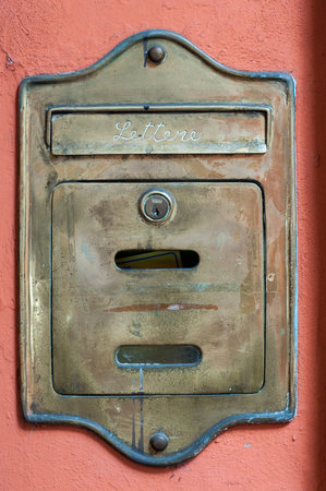 A weathered metal mailbox, marked â€œLettereâ€, is mounted on a vibrant red wall. The...