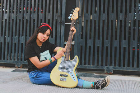 smilling young asian woman playing electric bass guitar in casual styleの写真素材