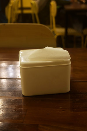 A white tissue holder is on a wooden table in a restaurant