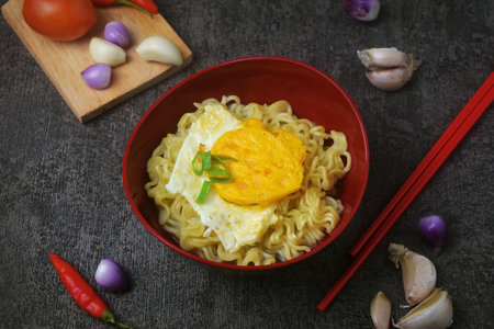 Closeup photo of a bowl of boiled noodles with fried egg that looks very delicious on a very elegant gray cement table mat, dark food photographyの写真素材