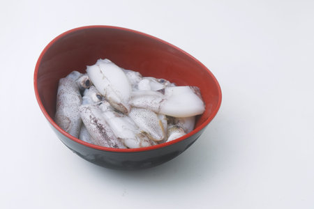 Raw and fresh squid is in a black bowl on an isolated white background.の写真素材