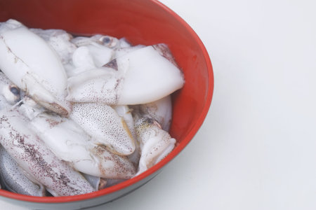 Close up and detail of raw and fresh squid in a black bowl with isolated white background.
